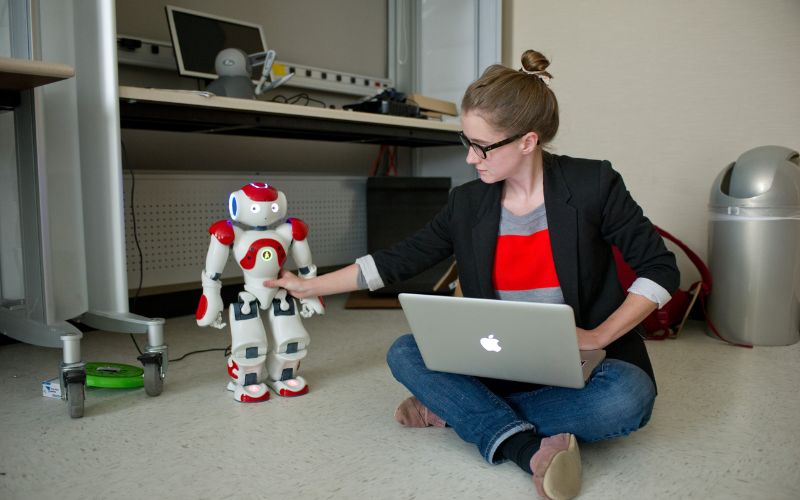 student sitting on the floor with a laptop working with a robot on the floor