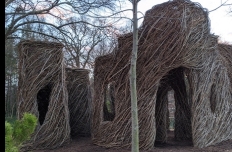 Thin saplings and branches have been woven together in the shape of cube-like buildings with arched doors and windows.